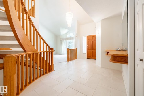 Foyer featuring light-toned tile flooring, a curved wooden staircase with balusters, a built-in wooden console, a prominent chandelier, and a paneled wooden entry door - 14 Highlands Place, Wetaskiwin, AB 