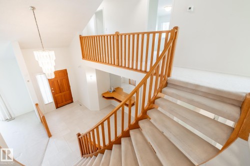 Two-story foyer with a chandelier, wood-finish front door, carpeted stairs, and a wood-finish railing - 14 Highlands Place, Wetaskiwin, AB 