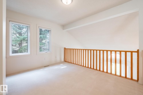 Open loft area featuring soft carpeting, two large windows, a wooden railing, and a flush mount light fixture - 14 Highlands Place, Wetaskiwin, AB 