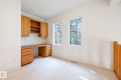 Built-in wood-finish desk with integrated cabinetry and shelving, two windows, wall-to-wall carpeting, and wood-finish railing - 14 Highlands Place, Wetaskiwin, AB 