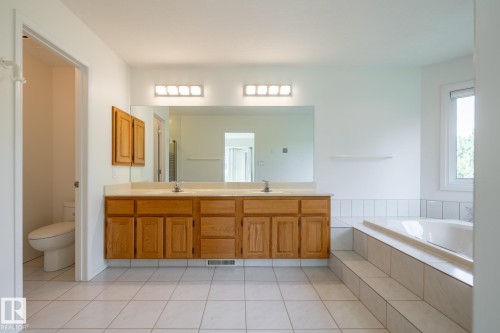 Dual vanity with wood-finish cabinetry, tile flooring, built-in soaking tub, and a window for natural light - 14 Highlands Place, Wetaskiwin, AB 