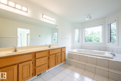 Dual vanity with oak-finish cabinetry, a large integrated mirror, and overhead lighting - 14 Highlands Place, Wetaskiwin, AB 
