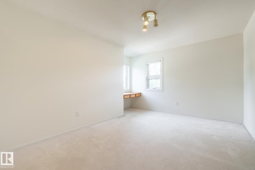 Built-in wood-finish desk, two windows with white trim, wall-to-wall carpeting, and a ceiling-mounted light fixture - 14 Highlands Place, Wetaskiwin, AB 