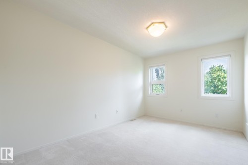 Bright interior space with light-colored carpeting, two windows with white trim, and a ceiling-mounted light fixture - 14 Highlands Place, Wetaskiwin, AB 