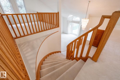 Curved staircase with wood railing, upper-level landing, and a tiered chandelier - 14 Highlands Place, Wetaskiwin, AB 