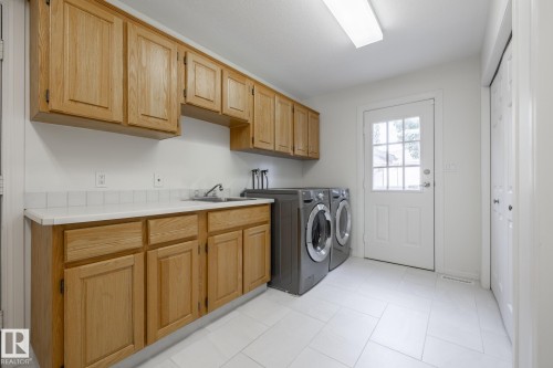 Light-toned wood cabinetry, white countertop, tile backsplash, stainless steel sink, and white tile flooring - 14 Highlands Place, Wetaskiwin, AB 