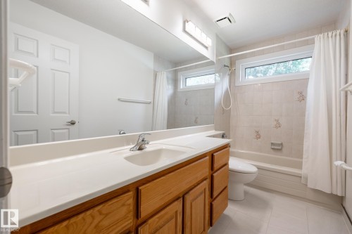 Full-width vanity with dual sinks, warm-toned wood cabinetry, and a large mirror - 14 Highlands Place, Wetaskiwin, AB 