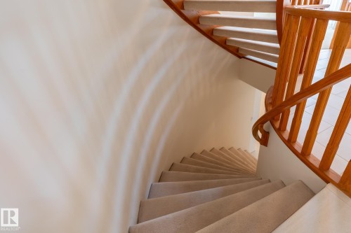 Curved staircase featuring wood balusters and handrail, carpeted treads, and light-toned wall finishes - 14 Highlands Place, Wetaskiwin, AB 