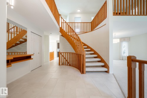 Grand foyer featuring a curved staircase with wood banister, light-toned tile flooring, and integrated wall shelving - 14 Highlands Place, Wetaskiwin, AB 