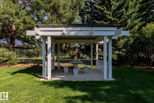 White gazebo with a concrete floor, built-in balusters, and a shingled roof, surrounded by mature trees and a manicured lawn - 14 Highlands Place, Wetaskiwin, AB 