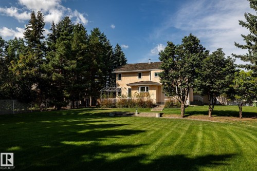 Expansive lawn with mature landscaping, featuring a two-story exterior, established trees, and a decorative garden structure - 14 Highlands Place, Wetaskiwin, AB 
