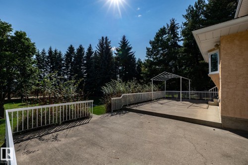 Concrete patio with white railing, featuring a white metal pergola frame and exterior stucco siding - 14 Highlands Place, Wetaskiwin, AB 