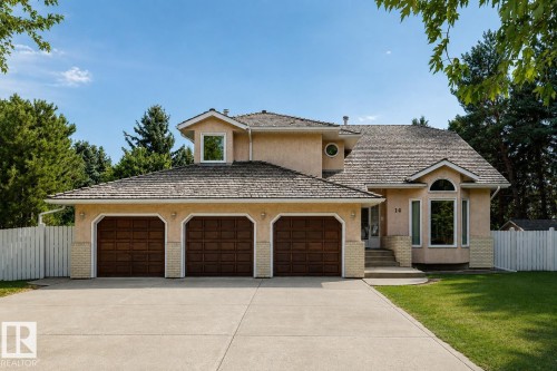 Stucco exterior with a peaked roofline, featuring a three-car garage with wood-finish doors, a concrete driveway, and a front entrance with a curved bay window - 14 Highlands Place, Wetaskiwin, AB 