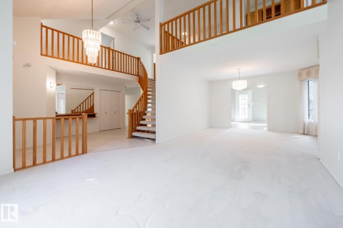 Voluminous living area with high ceilings, a spiral staircase with wood railings, an upper-level balcony, and a prominent chandelier - 14 Highlands Place, Wetaskiwin, AB 