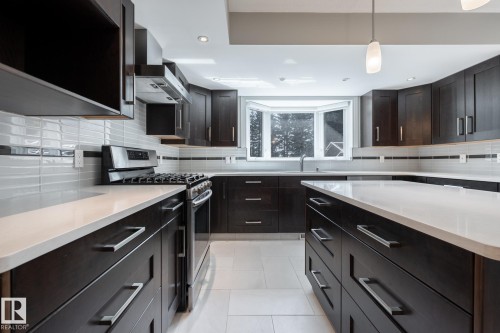 Kitchen featuring dark wood cabinetry, white countertops, stainless steel appliances, a tile backsplash, and a bay window with a sink - 14 Highlands Place, Wetaskiwin, AB 