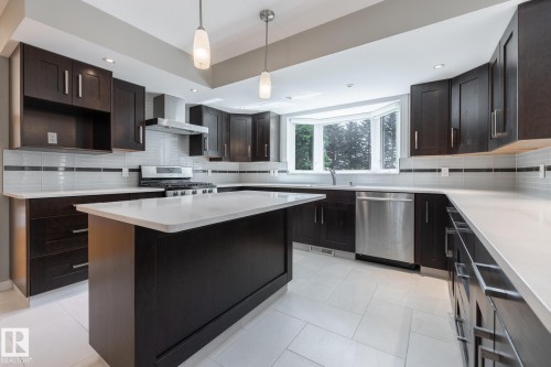 Kitchen featuring dark wood cabinetry, light countertops, stainless steel appliances, a center island, and a bay window - 14 Highlands Place, Wetaskiwin, AB 