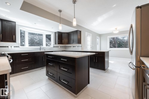 Kitchen featuring dark wood-finish cabinetry, light-toned countertops, a central island with storage, stainless steel appliances, and tile flooring - 14 Highlands Place, Wetaskiwin, AB 