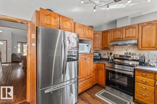 Wood-finish flooring, stainless steel appliances, track lighting, wood cabinetry, and dark countertops - 8015 158 Ave Nw, Edmonton, AB 
