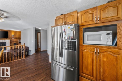 Wood-finish flooring throughout, stainless steel refrigerator, built-in microwave niche, and wood cabinetry with decorative hardware - 8015 158 Ave Nw, Edmonton, AB 