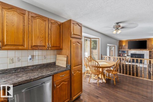 Kitchen featuring wood cabinetry, stainless steel dishwasher, tile backsplash, and dark countertops - 8015 158 Ave Nw, Edmonton, AB 