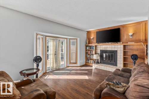Wood-finish flooring throughout, a fireplace with tile surround, built-in shelving, paneled accent wall, and a bay window with double doors - 8015 158 Ave Nw, Edmonton, AB 