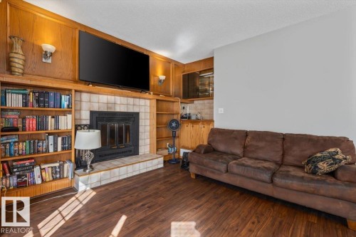 Wood-finish flooring, built-in shelving, tile-surround fireplace with hearth, wood paneling, and wall sconces - 8015 158 Ave Nw, Edmonton, AB 