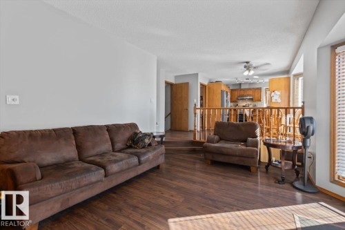 Wood-finish flooring, light grey wall paint, bay window with blinds, wooden railings, and ceiling fan in the background - 8015 158 Ave Nw, Edmonton, AB 