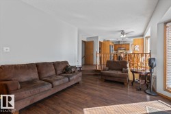 Wood-finish flooring, light grey wall paint, bay window with blinds, wooden railings, and ceiling fan in the background - 