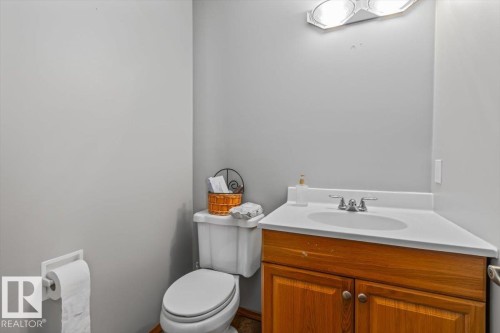 White toilet with a built-in toilet paper holder and a wood-finish vanity featuring a white countertop and integrated sink - 8015 158 Ave Nw, Edmonton, AB 