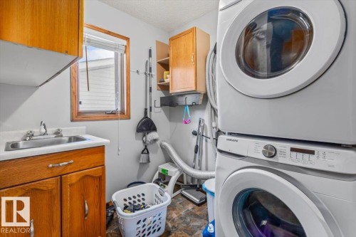Laundry area featuring a built-in sink, wood-finish cabinetry, and a stacked washer and dryer - 8015 158 Ave Nw, Edmonton, AB 