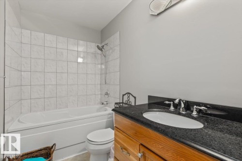 Bathtub with white tile surround, vanity with dark stone countertop, undermount sink, and wood-finish cabinetry - 8015 158 Ave Nw, Edmonton, AB 