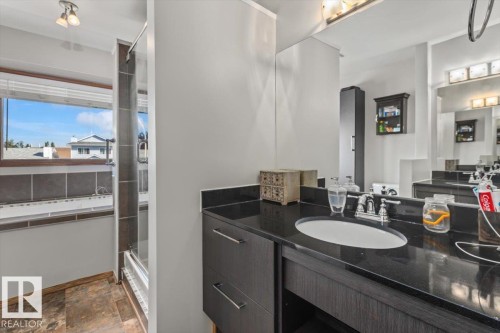 Vanity with dark countertop and undermount sink, large mirror, shower enclosure, and window with blinds - 8015 158 Ave Nw, Edmonton, AB 