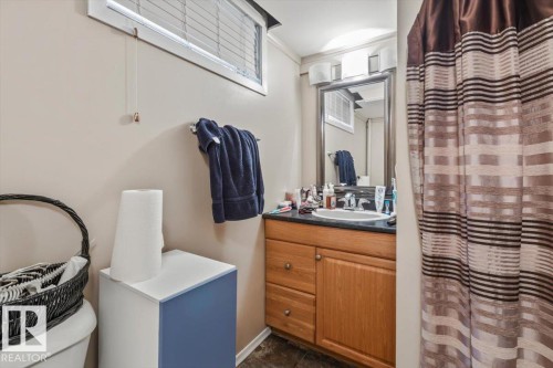 Bathroom with wood-finish vanity, dark countertop, and a framed mirror - 8015 158 Ave Nw, Edmonton, AB 