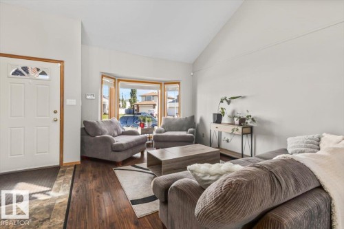 Vaulted ceiling, wood-finish flooring, bay window, light gray wall finishes, and a paneled entry door with transom window - 8015 158 Ave Nw, Edmonton, AB 
