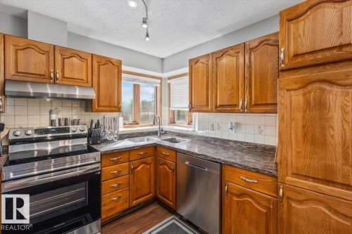 Wood cabinetry with stainless steel hardware, corner double basin sink, stainless steel dishwasher, stainless steel range with hood, and patterned countertops - 8015 158 Ave Nw, Edmonton, AB 