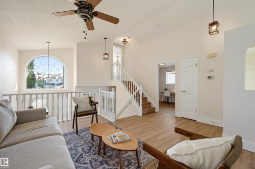 Vaulted ceiling with a decorative ceiling fan, arched window, wood-finish flooring, and white spindle railing staircase - 839 Blacklock Way Sw, Edmonton, AB 