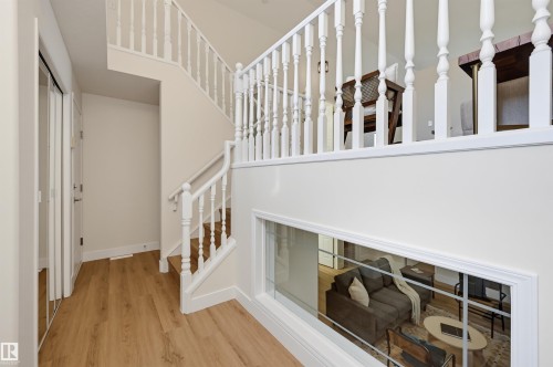Wood-finish flooring, white spindle staircase, upper-level balustrade, and a lower-level interior window - 839 Blacklock Way Sw, Edmonton, AB 