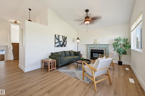 Vaulted ceiling, recessed fireplace with decorative tile surround, wood-finish flooring, ceiling fan, and window with roller shade - 839 Blacklock Way Sw, Edmonton, AB 