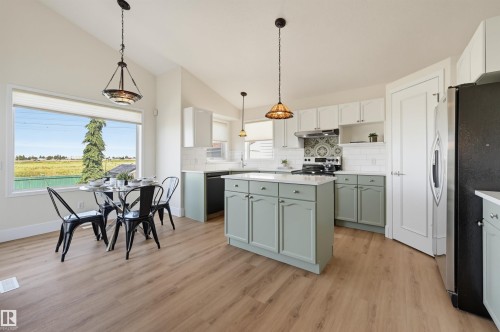 Kitchen featuring light wood-finish flooring, a central island with light green cabinetry, white subway tile backsplash, and a large window - 839 Blacklock Way Sw, Edmonton, AB 