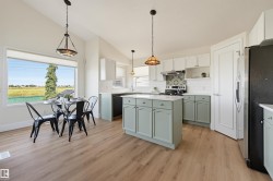 Kitchen featuring light wood-finish flooring, a central island with light green cabinetry, white subway tile backsplash, and a large window - 