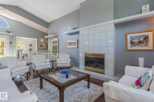 Vaulted ceiling, wood-finish flooring, tiled fireplace with brass trim, arched transom window, and white spindle railing - 8 Edgemont Point(E), St. Albert, AB 