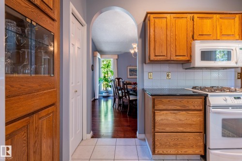 Kitchen featuring wood cabinetry, white tile flooring, black countertop, and a white tile backsplash - 8 Edgemont Point(E), St. Albert, AB 