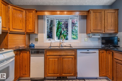Wood cabinetry with black countertops, a white tile backsplash, and a bay window - 8 Edgemont Point(E), St. Albert, AB 