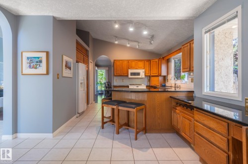Kitchen featuring warm wood cabinetry, solid surface countertops, white tile flooring, and vaulted ceiling with track lighting - 8 Edgemont Point(E), St. Albert, AB 