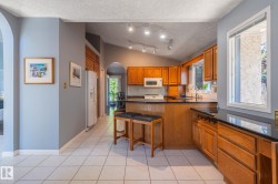 Kitchen featuring warm wood cabinetry, solid surface countertops, white tile flooring, and vaulted ceiling with track lighting - 