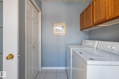 Dedicated laundry area featuring tile flooring, bi-fold closet doors, and overhead wood-finish cabinetry - 8 Edgemont Point(E), St. Albert, AB 