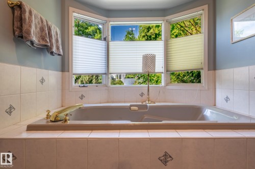 Built-in soaking tub with brass fixtures, surrounded by white tiled walls with decorative accents - 8 Edgemont Point(E), St. Albert, AB 