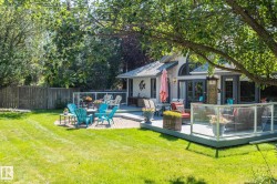 Expansive backyard featuring a manicured lawn, a multi-level deck with glass railings, a brick patio, and mature trees providing natural shade - 