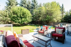 Expansive backyard featuring a large deck, mature trees, and a manicured lawn - 