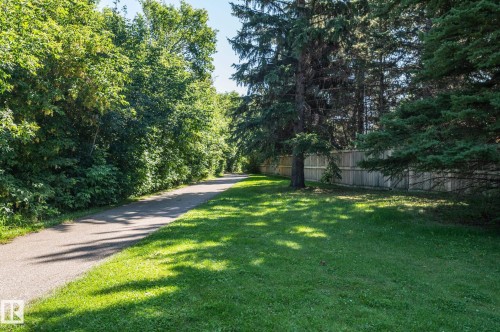 Paved pathway bordered by mature trees and a manicured lawn, featuring a wood privacy fence - 8 Edgemont Point(E), St. Albert, AB 